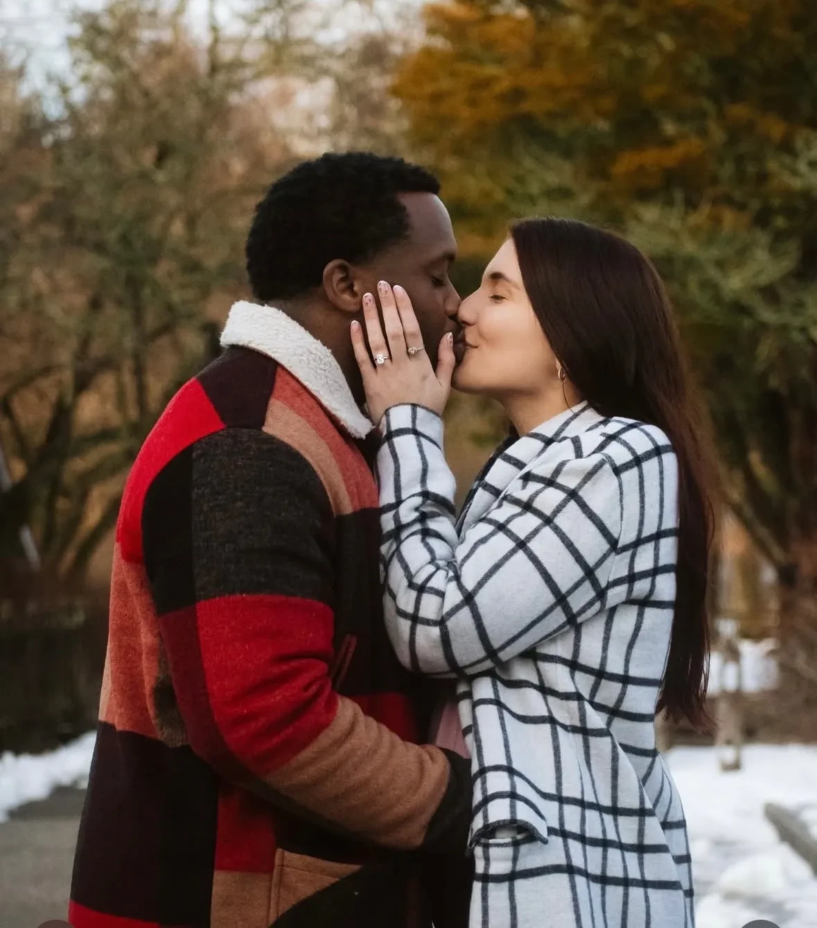 Couple sharing a kiss showing engagement ring in winter park