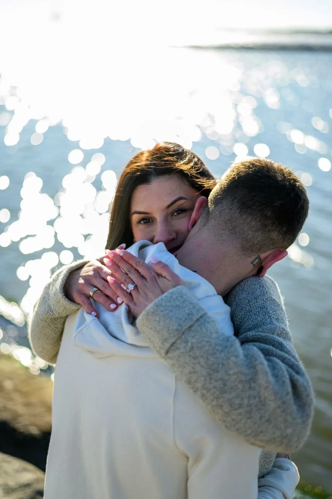 Couple hugging by the water showing engagement ring